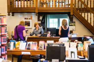 The interior of the Hills Branch library. Library patrons talk with the librarian behind the front desk.
