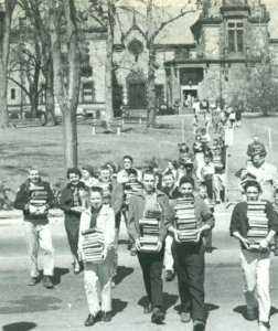 Operation Bookswitch. Many people carry stacks of books, crossing the street in front of the town hall building.
