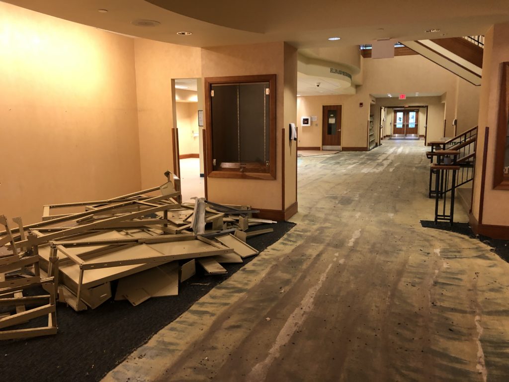 The New Titles area with the metal shelving scattered on the floor. The welcome area is also visible and has noticeably bare concrete floors.