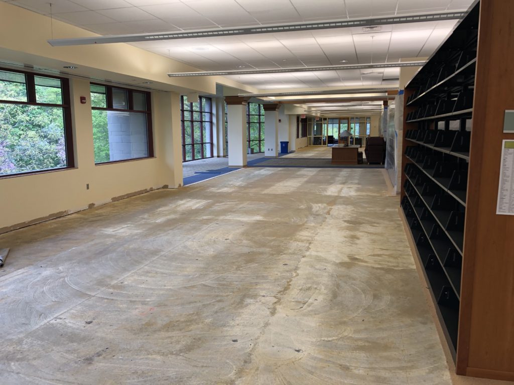 The second floor area on the park-facing side of the building with carpet removed. There are subtle lighter spots on the floor where shelving once was. 