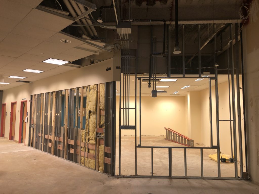 A view of the Middle School Room, with a stripped wall showing where the LUMES installation will go. Another wall is just its metal struts, with a large opening for the new window looking into the room.