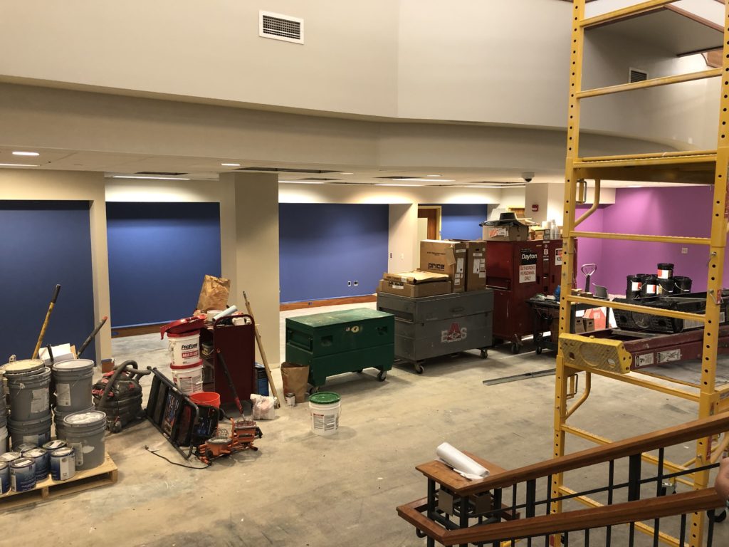 The place that will become the Welcome Center, still without carpeting, but now with clean, dark blue and magenta paint on the walls. Painting supplies stacked on the floor indicate it was done recently.