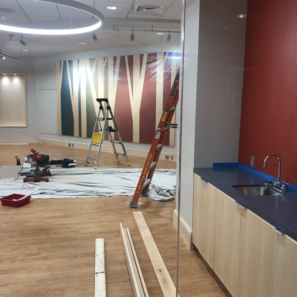 Art on wood, with abstract tree branch patterns blocked out by a muted blue to red rainbow has been installed on the Common's wall. Also visible is the new sink, and new wood flooring.
