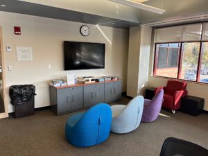 Three chairs sat in front of the High School Room TV. Board games are on the cabinets underneath the TV.