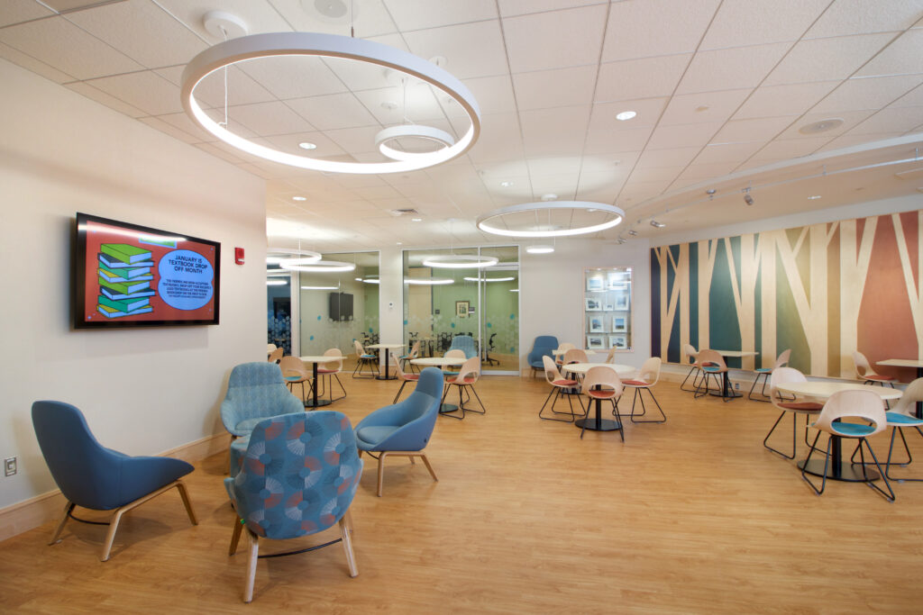 The newly-renovated Commons area with a handful of tables where patrons may eat food and talk to each other. There are also two rooms- a meeting room and a conference room- for patrons to use, and a display advertising library events.