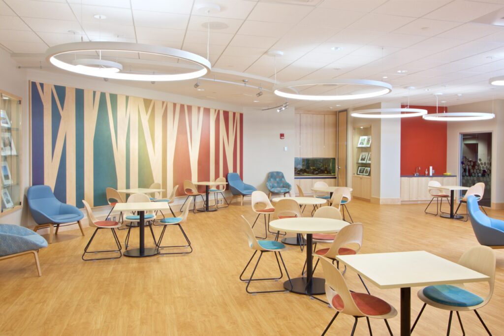 Another view of the Commons, showcasing the tables and chairs for patrons to use. Along the back wall is a colorful wooden mural of stylized trees.
