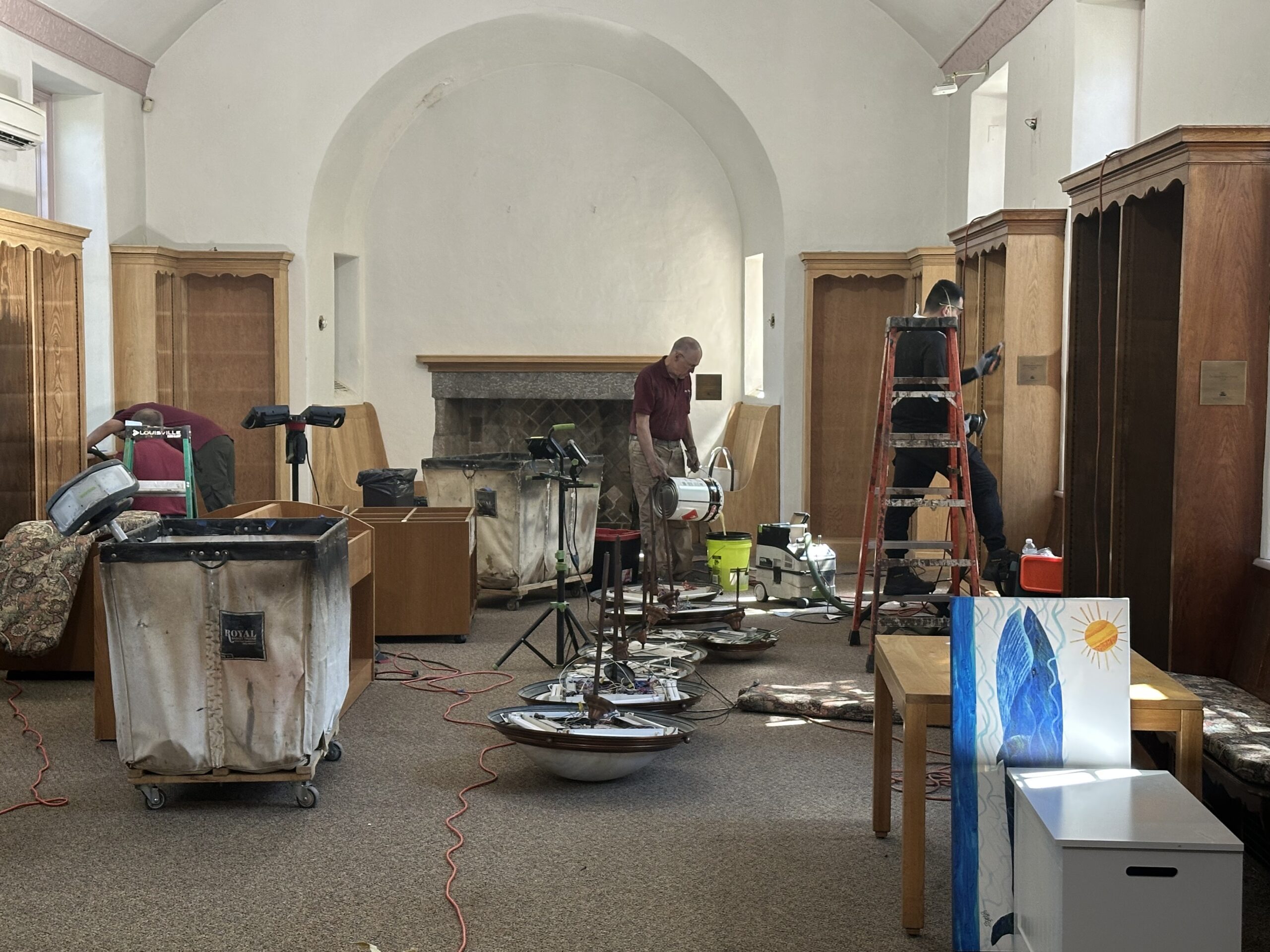 LIbrary space empty of books, with lighting fixtures taken down and tarps and painting materials available.