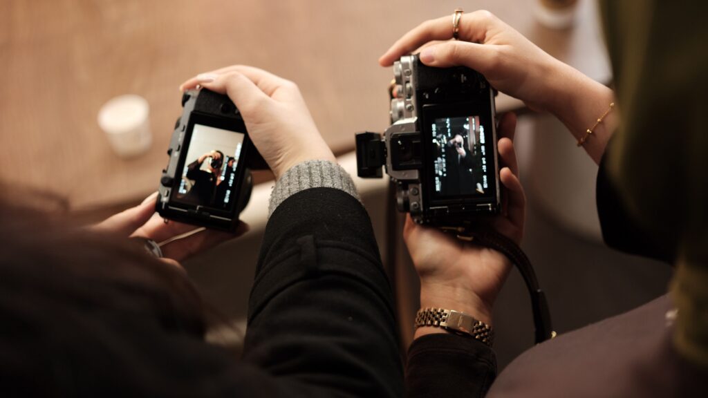 The image features two individuals holding cameras, positioned closely together.