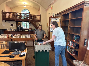 Two library staff emptying shelves by packing books into gray boxes at the Hills Branch.